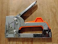 Metal and orange plastic Arrow stapler model T2025 with lever handle, shown from side angle.