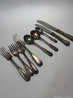 Flatware pieces laid out showing knives, forks, spoons with tarnish and wear, on white background