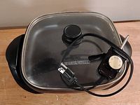 Top view of the electric frying pan showing glass lid with Black & Decker logo and attached power cord with dial temperature control.