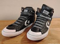 Front angle view of black and white Converse All Star high top sneakers showing velcro strap, laces, and logos