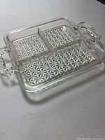 Photo of square pressed glass dish with four dividers and ornate handles, showing starburst patterned base.