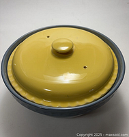 Top view of covered casserole dish showing yellow lid with knob and ventilation holes on blue base.