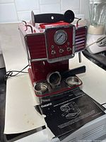 Red Galanz machine with manual underneath on counter, portafilter holder attached mid-position, steam wand on side.