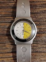 Top view of the men's Omax watch showing the round dial with yellow and white segments and silver strap with circular perforations.