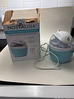 Front view of Nostalgia electric ice cream maker alongside original product box, showing condition and packaging