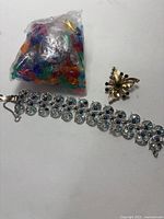 Silver-tone bracelet laid flat with visible blue and clear stones, some stones missing, next to gold-toned brooch shaped decoratively.