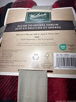 Close-up of Woolrich product label identifying the throw as Plush to Sherpa Throw, 60" x 70", 100% polyester, OEKO-TEX certified.