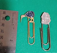 Two oversized decorative paperclip bookmarks; one shaped as a kiwi bird with blue textured body and the other as a silver birdhouse, shown next to a ruler for size reference about 3 inches long.