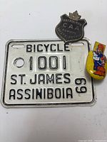 Front view of the bicycle license plate, patrolman badge, and yellow clicker showing details
