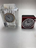 Two clocks side by side on a white background: Waterford Crystal clock and red Seiko alarm clock.