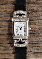 Close-up image of rectangular women's Avon quartz watch with rhinestones on top and bottom of case, black strap, white dial with Roman numerals.