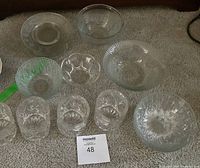 Eleven piece glassware set including bowls and tumblers, all with intricate cut glass patterns, arranged on carpet floor.