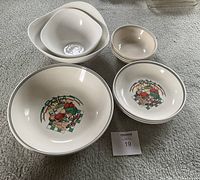 11 piece set of white ceramic bowls with pasta-themed designs and plain bowls arranged on carpeted floor.