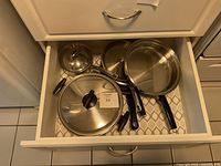 Top-down view of the cookware set inside a kitchen drawer showing three pots and pans with handles and two lids.
