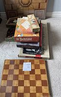 Stack of board game boxes including Yahtzee, Scrabble, Over the Hill Bingo, Monopoly, Win-A-Lot, with two wooden game boards in front on carpeted floor.