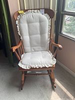 Front view of the classic wooden rocking chair with white fabric cushions showing the brown wood frame and cushioned seat and backrest.