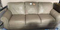 Front view of the taupe leather 3-seater couch showing three seat and back cushions with minor wear.