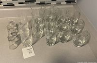 20-piece glassware set arranged on kitchen countertop, includes multiple highball glasses and short tumblers, clear and transparent with simple design.