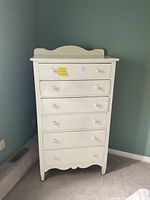 Front view of the white wooden tall dresser with six drawers, showing the traditional styled scalloped base trim and curved top edge with round knobs on each drawer.