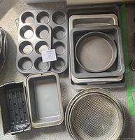 Full view of the metal bakeware set laid out showing various pans including muffin tin, baking sheets, round cake pans, loaf pan, and pizza pan.