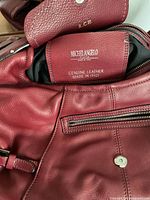 Close-up photo showing Michelangelo Firenze brand label inside a red genuine leather handbag with visible black lining and magnetic snap closure on flap.