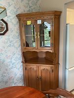Full view of the oak corner cabinet showing upper glass door storage and lower solid door storage.