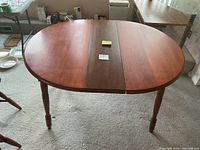 Oval wooden dining table with darker center leaf expanded, showing oval shape and wooden grain surface.