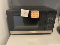 Front view of Panasonic microwave showing black glass door and stainless steel handle area with note displaying dimensions.