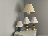 Four vintage lamps arranged together, showing a variety of table and hanging lamps with matching lampshades and bulbs.