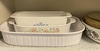 Photo showing three white ceramic rectangular baking dishes stacked inside one another with varied floral patterns, including multicolor and blue flowers, and one plain ridged dish.