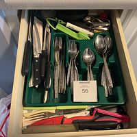 Full view of the drawer with green plastic organizer tray holding various kitchen utensils including forks, spoons, knives, peelers, and tongs.