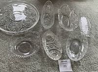 Top-down view of all 7 vintage crystal pieces arranged on carpet showcasing variety of shapes and cut engraved patterns.