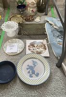 Collection of assorted vintage ceramic and glassware displayed on carpet, including a large Mickey Mouse plate at front, assorted small plates, decorative jars, and glass vases.