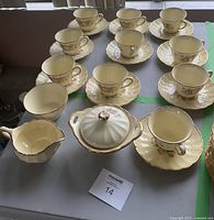 Full view of the vintage tea set including 8 cups, 8 saucers, a creamer, and a lidded sugar dish, all with 18K gold trim and floral design.