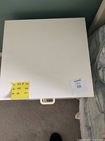 Top view of white wooden nightstand showing flat surface with a drawer handle visible at the bottom edge, with sticky note indicating dimensions.