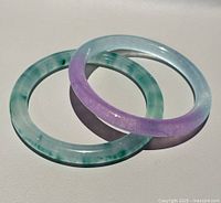 Lavender and green jade bangles overlapped on flat surface