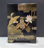 Front view of closed lacquer jewelry cabinet showing painted crane and lotus motifs and brass hardware