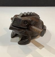 Angled view of carved frog guiro with striker in mouth