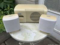 Front view of powered subwoofer with integrated speaker and two satellite speakers on round table outdoors.