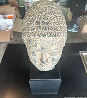 Top-front view of the Buddha head bust showing the textured curled hair detail and serene facial expression, mounted on black square base.