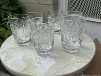 Set of six cut crystal highball glasses arranged on round tabletop showing starburst and fan cut pattern.