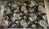 Full view of the floral carpet laid on the floor showing the black background with beige flower motifs and leaf vines.