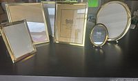 Seven photo frames of various sizes and shapes arranged on a flat surface showing gold solid brass finish with reflective lacquer coating
