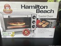 Photo of box showing Hamilton Beach toaster oven with pizza inside, front view featuring 4 slice capacity and other features.
