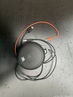 Compact black JBL portable speaker with attached auxiliary cable lying on a black surface.
