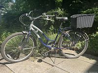 Full side view of the silver and navy Schwinn cruiser bike showing frame, rear basket, pedals, tires, and handlebar.