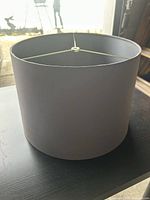 Side view of a clean, modern drum-style black or dark grey lampshade showing exterior and slight rim wear.