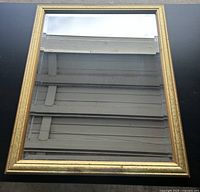 Photo shows a framed mirror with gold-colored decorative frame, reflecting ceiling beams.