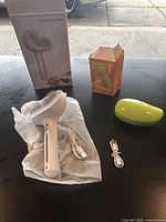 Photo of pink pet spray hair comb with brush, USB charging cable, water spray bottle, and original packaging box, alongside green silicone massage brush with charging cable and original box