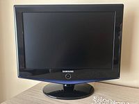 Front view of the black Samsung 19-inch widescreen LCD TV on its stand showing screen and front panel with Samsung logo and power button.